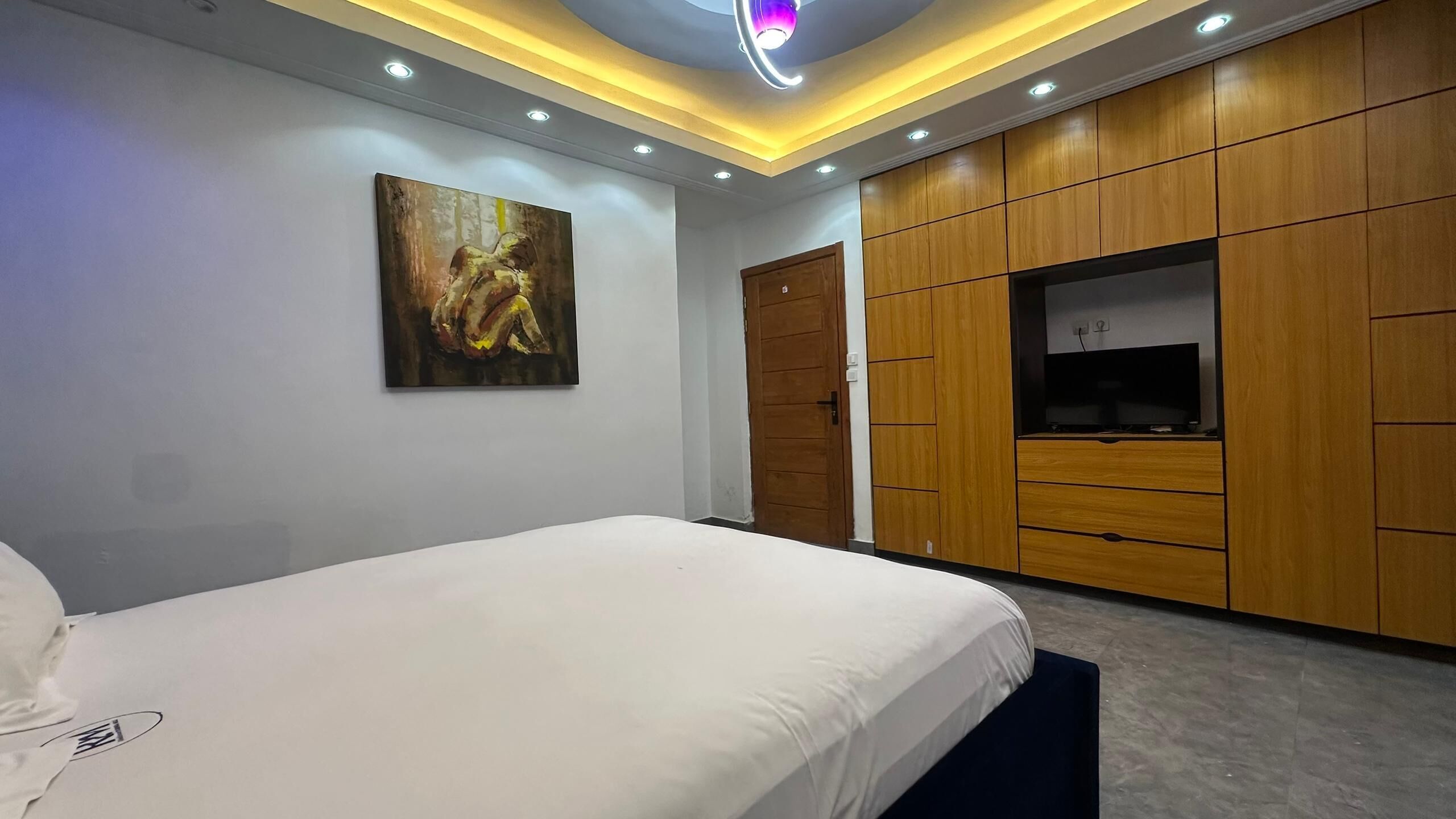 Ein Schlafzimmer mit einem Bett, einem Gemälde, einem Holzschrank und einem Fernseher.