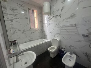 A bathroom with a marble wall, a toilet, a bidet, and a sink. - Tchinda Meli Residence (Douala)