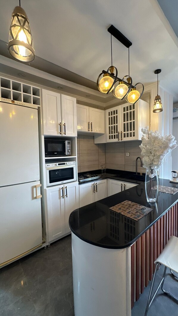 A modern kitchen with white cabinetry, a black countertop, and pendant lighting. - Tchinda Meli Residence (Douala)