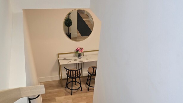 Een trap met houten treden leidt naar een eethoek met een ronde spiegel, een tafel en twee stoelen.