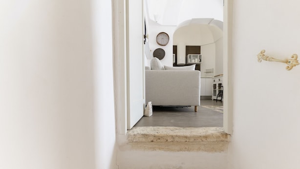 A narrow hallway leading to a room with a bed, a round wall clock, and a decorative door handle.
