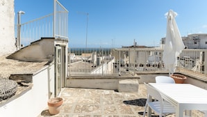 A rooftop terrace with a white table and chairs, a white umbrella, and a view of the sea.