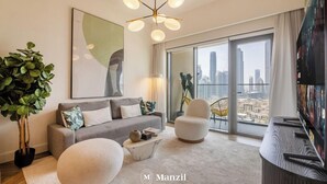 Un salon moderne avec un canapé gris, un pouf rond, une table basse et une grande fenêtre donnant sur la ville.