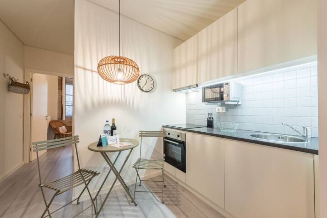 A modern kitchen with a dining area, featuring a round table, two chairs, a hanging light fixture, a clock, and a built-in oven.