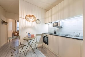 A modern kitchen with a dining area, a hanging light fixture, a clock, and a built-in oven.