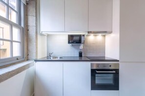 A modern kitchen with white cabinets, a built-in microwave, a stainless steel oven, and a window. - Guestready - Genuine Residences (Porto)