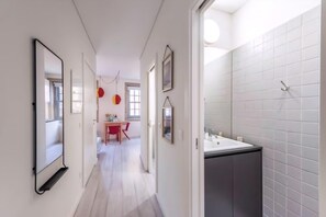 A hallway with a mirror, a dining area with a red chair, and a bathroom with a sink and tiled walls. - Guestready - Genuine Residences (Porto)
