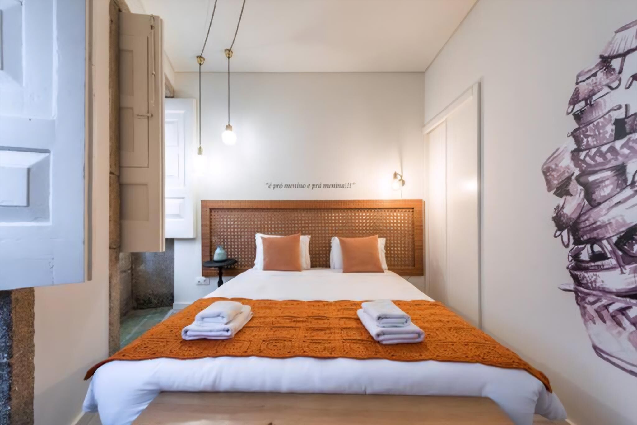 Quarto de hotel com uma cama grande, cabeceira de madeira e uma parede com uma frase.