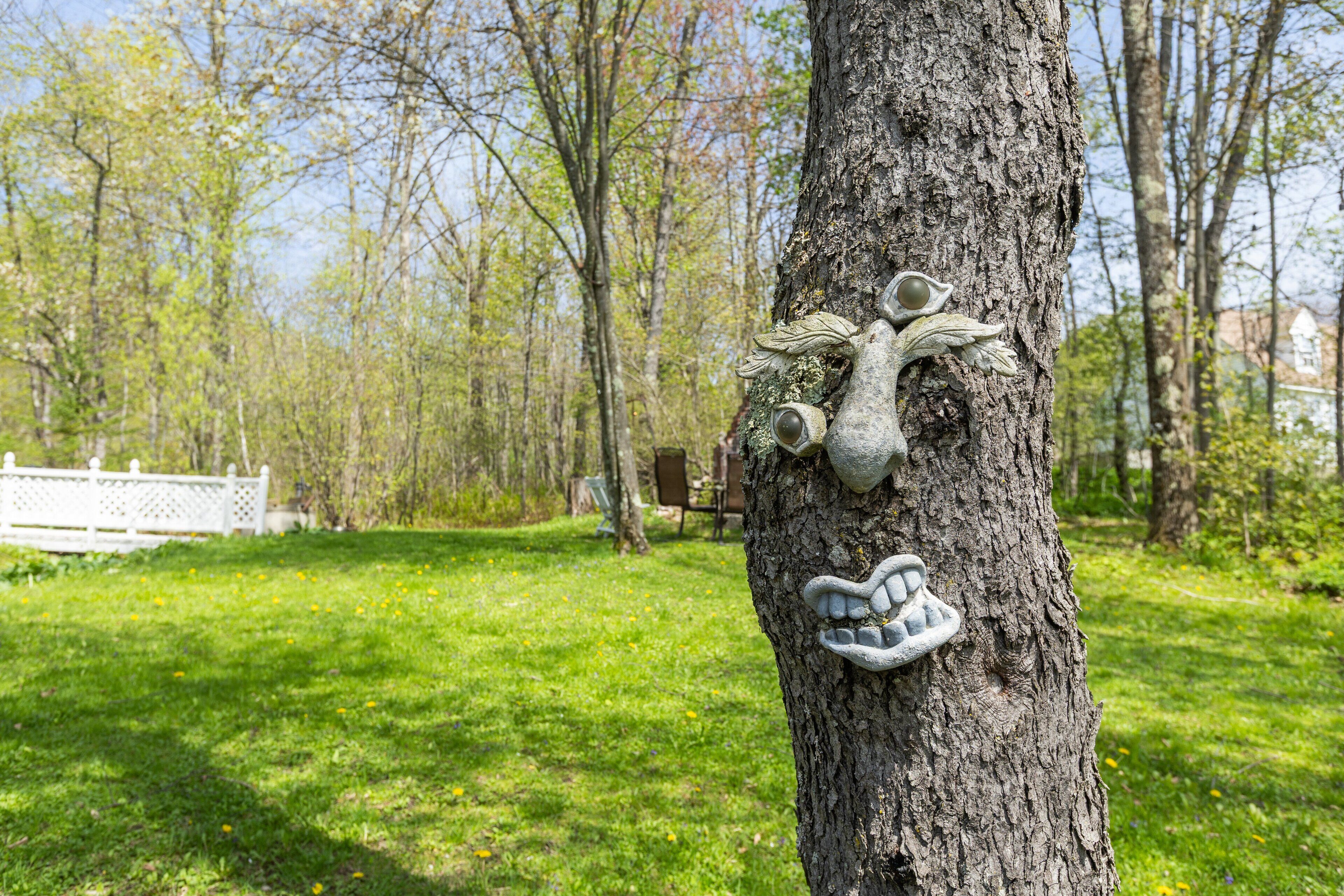 A tree with a carved face and a handprint, surrounded by a grassy area and trees.