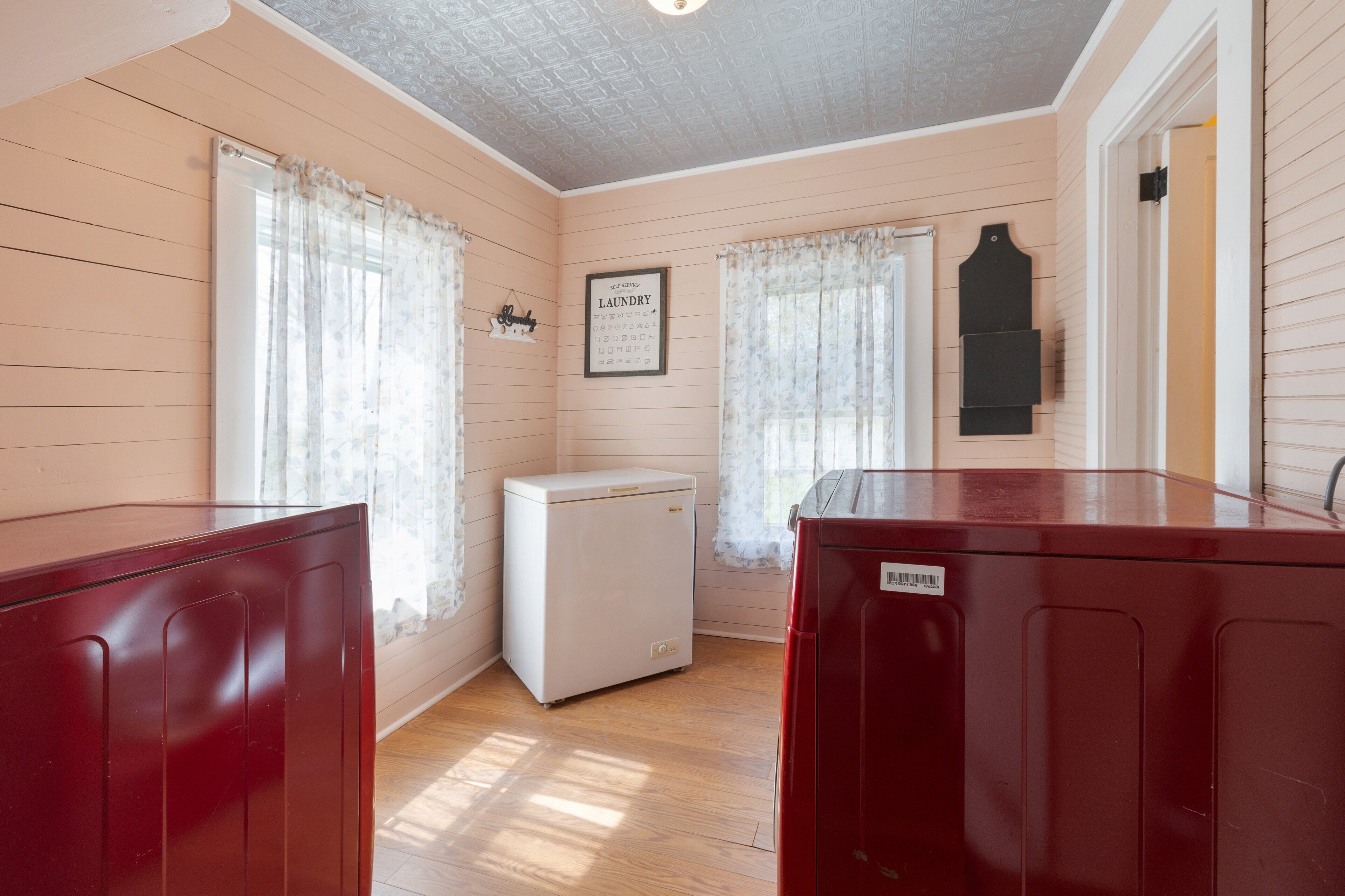 A room with wooden walls and floors, a small white refrigerator, and a red cabinet.