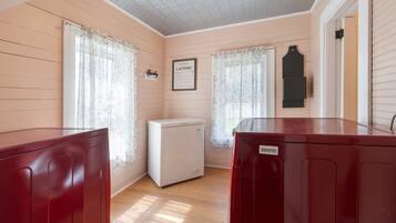 A room with wooden walls and floors, a small white refrigerator, and a red cabinet.