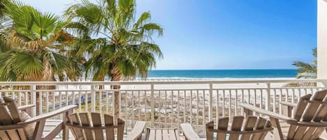 A balcony with wooden chairs and a view of the beach and ocean.