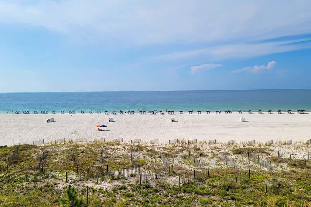 Ein Strand mit sandigem Ufer, einer Umzäunung und blauem Himmel.