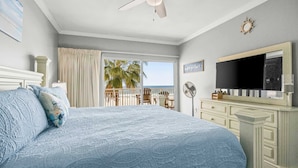 Ein Schlafzimmer mit einem großen Bett, einem Fernseher, einer Kommode und einem Balkon mit Meerblick.