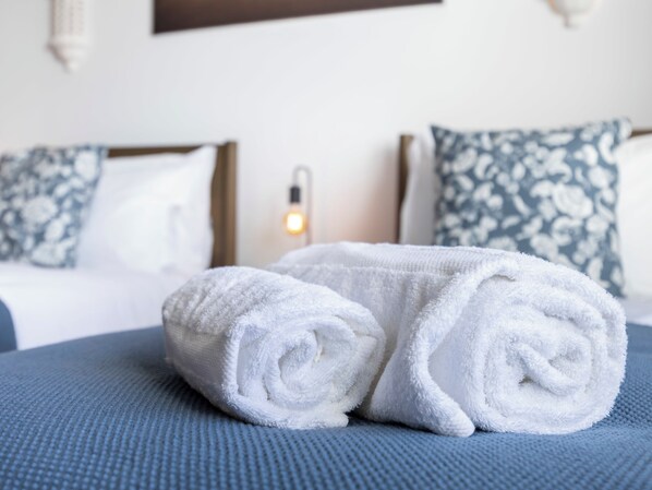 Ein ordentlich bezogenes Bett mit weißen Handtüchern, einer blauen Bettdecke und Kissen mit Blumenmuster.