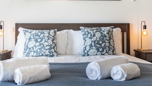 A neatly made bed with floral pillows, two bedside lamps, and a mountain landscape painting above it. - Apartment do Ramses with oceanviews (Luz)