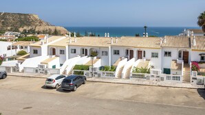 A coastal residential area with white buildings, a paved road, and parked cars. - Apartment do Ramses with oceanviews (Luz)
