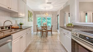 A modern kitchen with white cabinetry, granite countertops, and a central island with chairs. - Adorable Villa close to beach and tennis (Kiawah Island)
