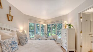 A bedroom with a large bed, two chairs, a dresser, and a window with a view of trees. - Adorable Villa close to beach and tennis (Kiawah Island)