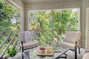 A covered outdoor seating area with two cushioned chairs, a glass table, and a pitcher of lemonade.
