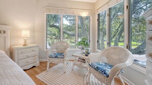 A bedroom with a large window, a bedside table with a lamp, two wicker chairs, and a view of trees outside. - Adorable Villa close to beach and tennis (Kiawah Island)