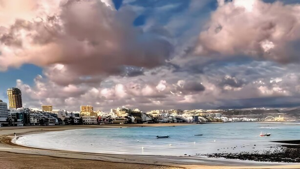 Un paisaje urbano costero con playa, edificios y cielo nublado.