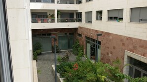 Un edificio de varios niveles con balcones, un patio con plantas y una combinación de paredes de vidrio y ladrillo.