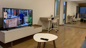 Una sala de estar moderna con un televisor de pantalla plana, una mesita pequeña, un escritorio y una silla.