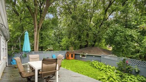 Eine Holzterrasse mit Tisch und Stühlen, umgeben von einem üppigen grünen Garten und einem Holzzaun.
