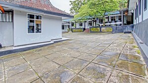 A courtyard with stone tiles, traditional buildings with tiled roofs, and a tree. - OYO 92287 Hotel Aji Mantoro (Belik)