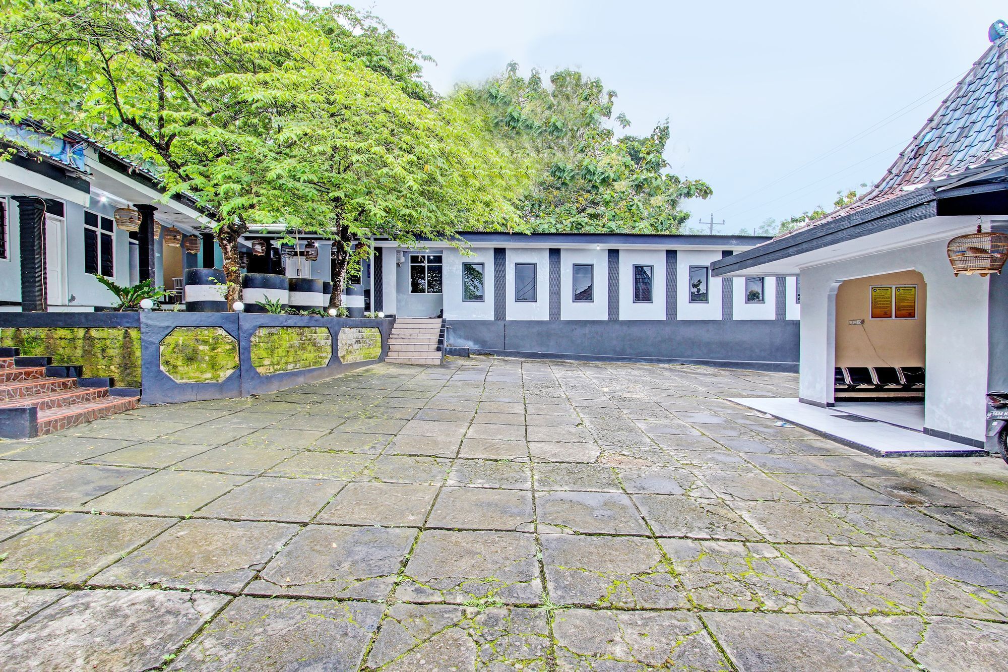 A courtyard with stone paving, a building with a tiled roof, and a staircase leading to a door.