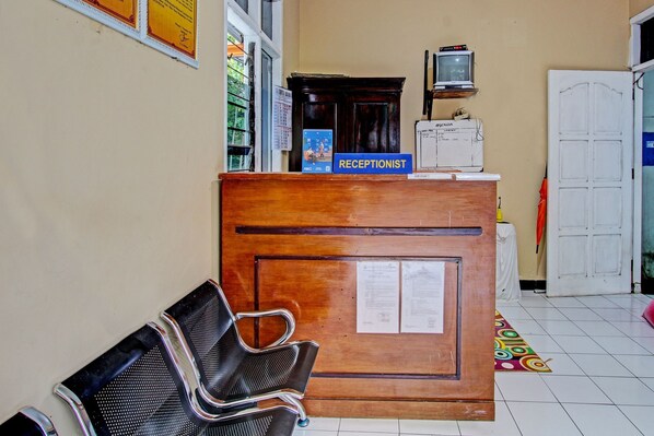 A reception desk with a sign reading "RECEPTIONIST," a wooden counter, a television, and a door in a hallway. - OYO 92287 Hotel Aji Mantoro (Belik)