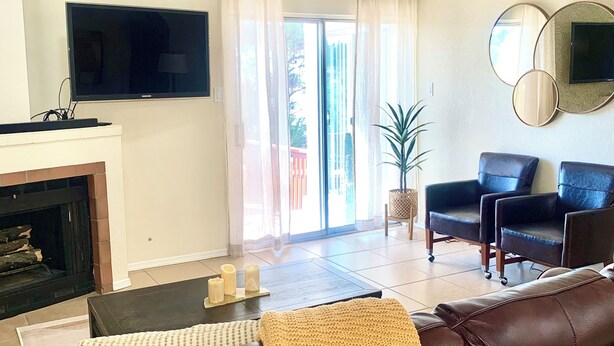 Een woonkamer met een bruine leren bank, een flatscreen televisie, een plafondventilator, een open haard en een schuifpui naar een balkon.