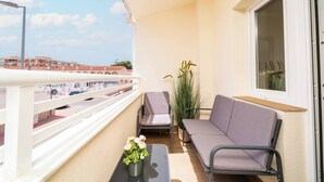 Ein Balkon mit einer Couch, zwei Stühlen, einem kleinen Tisch mit Pflanze und einem Fenster mit Blick auf Gebäude.