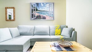 Ein Wohnzimmer mit einem hellgrauen Sofa, einem Holztisch, einem Bild von einer Strandlandschaft und einem gerahmten Spiegel an der Wand.