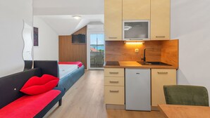 A compact hotel room with a kitchenette, a bed with red pillows, a sofa, and a view of the outdoors.