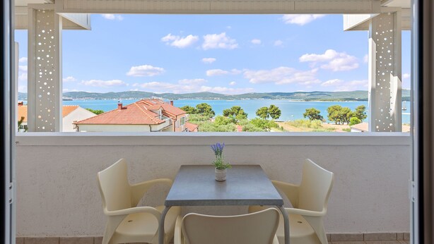 A balcony with a table and chairs, overlooking a coastal landscape with houses and trees.