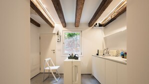 A compact kitchen with a window, a white chair, and a countertop with appliances. - Venice • Private Court / Peggy Cozy Apartment (Venezia)