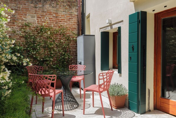 A patio with a glass table and red chairs, a brick wall, and a green door.