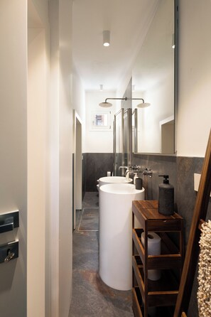 A modern bathroom with a white sink, a wooden shelf with toiletries, and a large mirror.