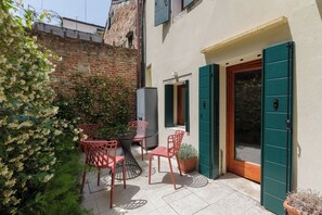 A patio with a table and chairs, a potted plant, and a door with green shutters.