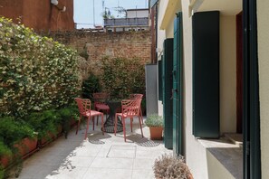 A small outdoor patio with a table and four chairs, surrounded by potted plants and a brick wall.