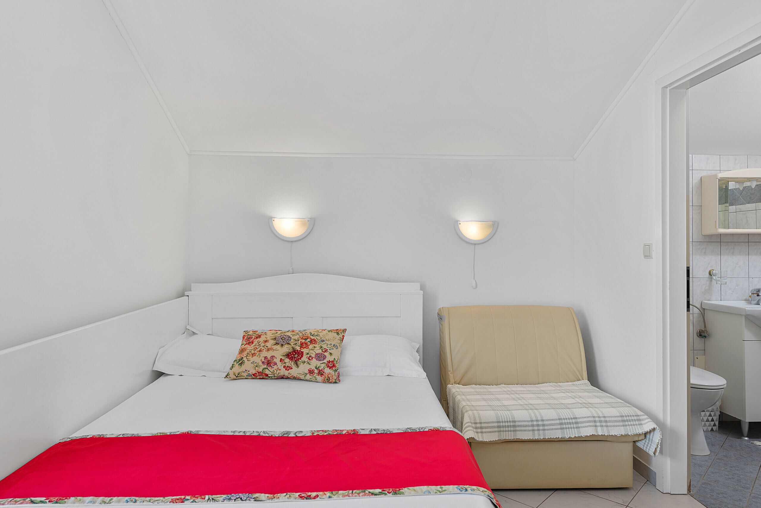 A bedroom with a bed, a chair, a nightstand, and a bathroom visible through an open door.