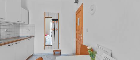 Una cocina moderna con armarios blancos, encimera de madera y un taburete pequeño. Hay un comedor con mesa, sillas y un jarrón con flores.