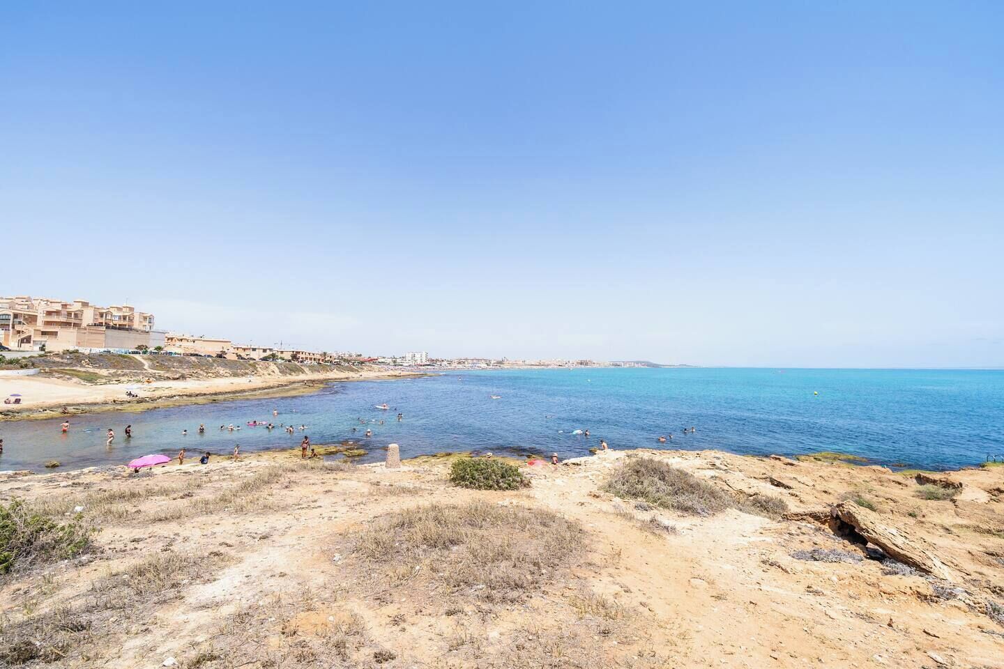 A coastal area with a sandy beach, rocky terrain, and a clear blue sea.
