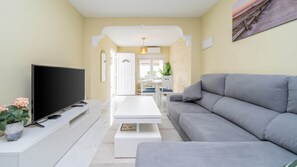 Un soggiorno con una TV a schermo piatto, un divano grigio, un tavolino da caffè bianco e una zona pranzo con tavolo e sedie.