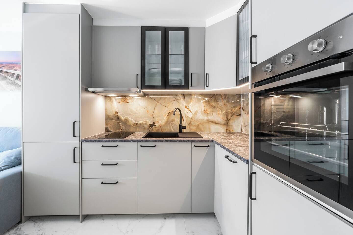A modern kitchen with white cabinetry, a marble backsplash, and a built-in oven.