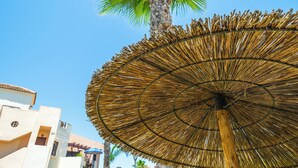 Une structure en forme de parasol à toit de chaume, avec un palmier en arrière-plan.