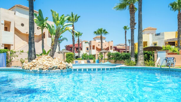 Une piscine à l’eau d’un bleu cristallin, entourée de palmiers et bordée d’un bâtiment doté de balcons.