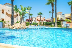 Une piscine à l’eau d’un bleu cristallin, entourée de palmiers et bordée d’un bâtiment doté de balcons.